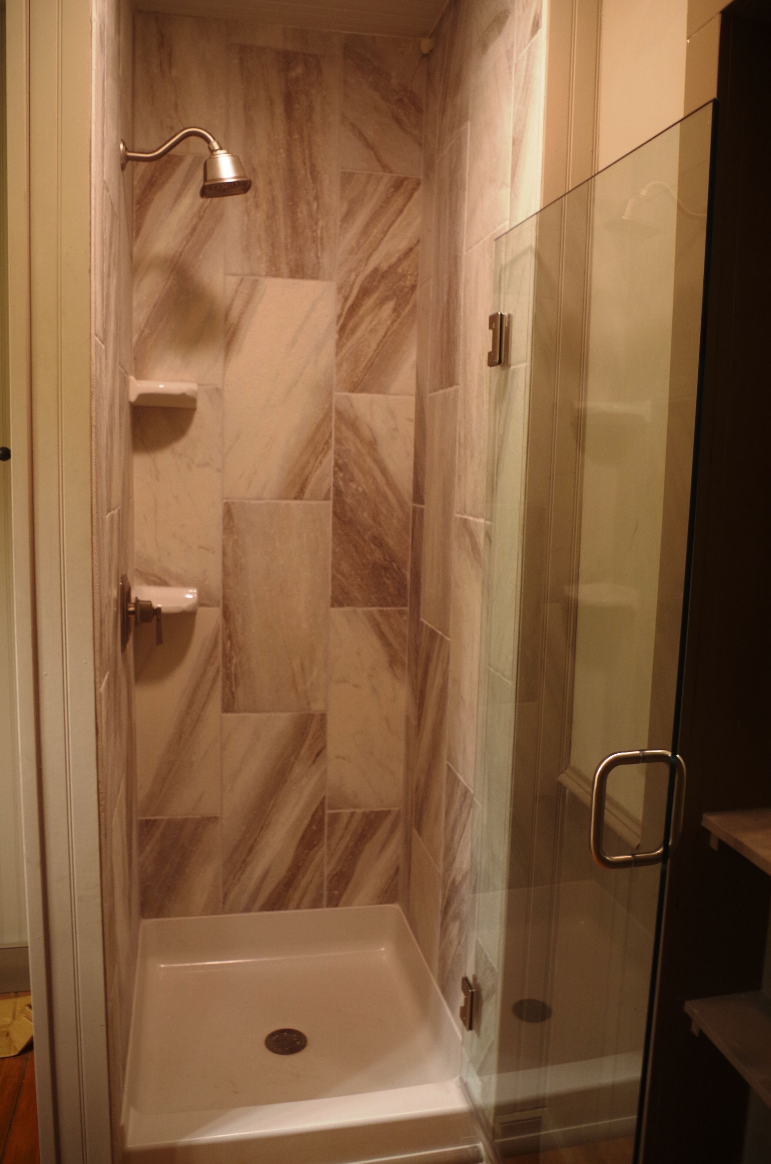 A walk-in shower with a glass door, marble tiles, and a handheld showerhead.