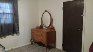 Una habitación con un aparador de madera, un espejo, una puerta oscura y una ventana con cortinas.