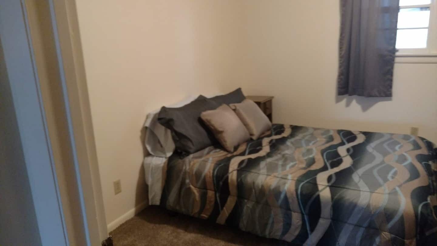 Ein Schlafzimmer mit einem Bett, Kissen und einem Fenster mit Vorhängen.