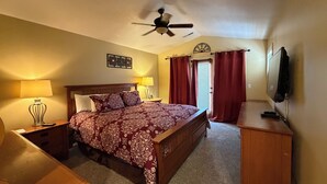 Une chambre à coucher avec un lit, des lampes de chevet, un ventilateur de plafond, une télévision et une fenêtre avec des rideaux.