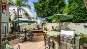 An outdoor patio with a grill, two umbrellas, and a stone fire pit. - Beautiful Ocean View (San Clemente)