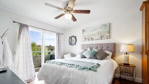 A bedroom with a bed, a ceiling fan, a nightstand, a lamp, and a view of the outdoors. - Beautiful Ocean View (San Clemente)