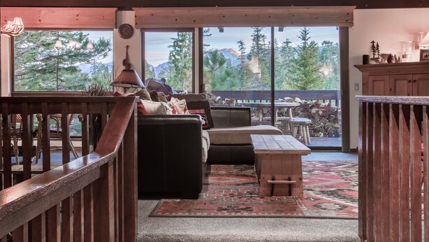 A cozy living room with a leather sofa, a wooden coffee table, and a large window offering a mountain view.