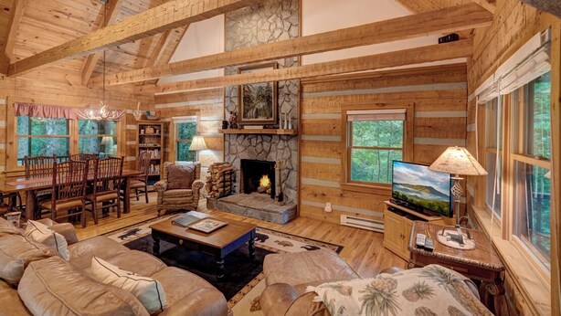 A log cabin interior with a fireplace, wooden furniture, and large windows. - Arroyito-Mtn Cabin, Pet-Friendly, Wood Fireplace, Shared Firepit, Charcoal Grill (Seven Devils)