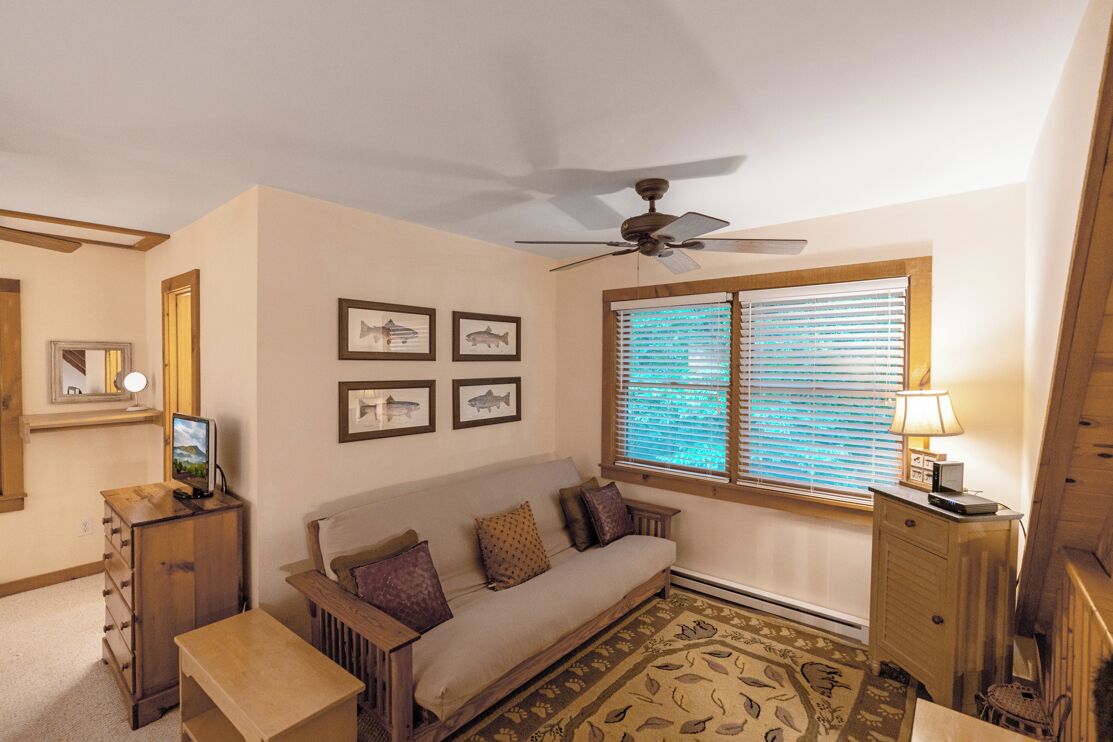 A cozy living room with a sofa, a small table, a ceiling fan, and framed fish pictures on the wall.