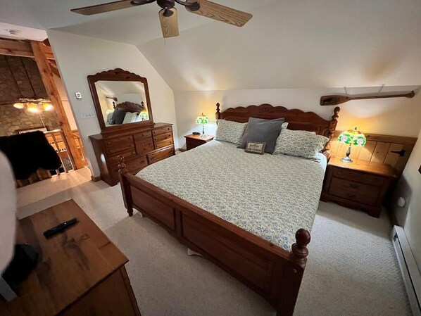 A bedroom with a large bed, wooden headboard, two bedside tables with lamps, a dresser, and a ceiling fan.