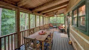 A wooden deck with a table and chairs, surrounded by large windows offering a forest view. - Arroyito-Mtn Cabin, Pet-Friendly, Wood Fireplace, Shared Firepit, Charcoal Grill (Seven Devils)