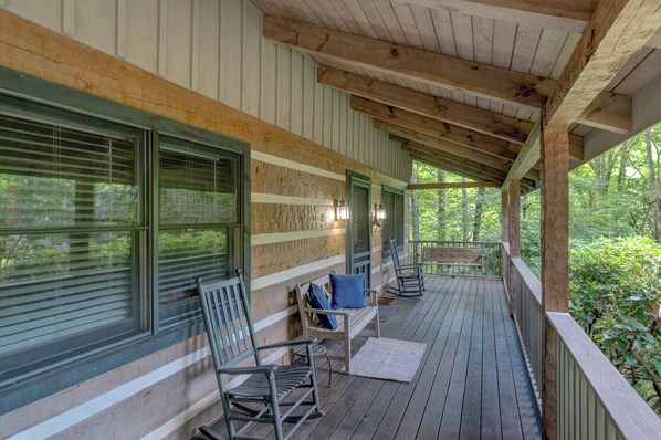 A covered porch with wooden flooring, metal railings, and a bench with cushions.