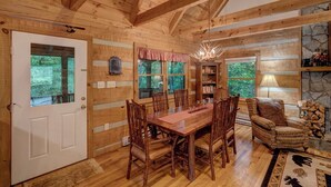 A wooden cabin interior with a dining table, chairs, a fireplace, and a stone wall. - Arroyito-Mtn Cabin, Pet-Friendly, Wood Fireplace, Shared Firepit, Charcoal Grill (Seven Devils)