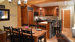 A kitchen with wooden cabinets, a dining table with chairs, a chandelier, and a microwave.