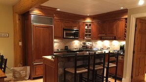 A kitchen with wooden cabinets, a central island with bar stools, a microwave, and a refrigerator.
