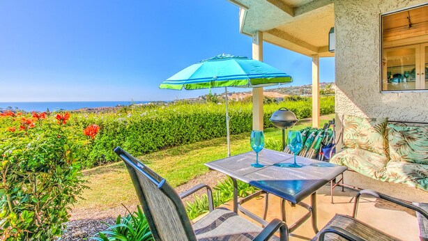 Een buitenterras met een tafel, stoelen, een blauwe parasol en uitzicht op de oceaan.