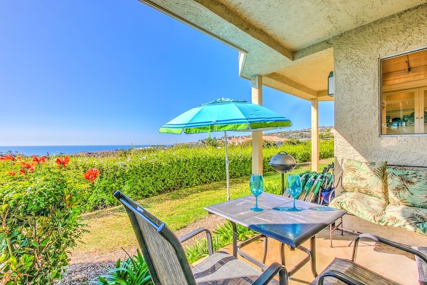 An outdoor patio with a table and chairs, a blue umbrella, and a view of the ocean. - UNOBSTRUCTED OCEAN-GOLF Views, step in shower, KING bed, garage, Gym
STR14-0115 (DANA POINT)