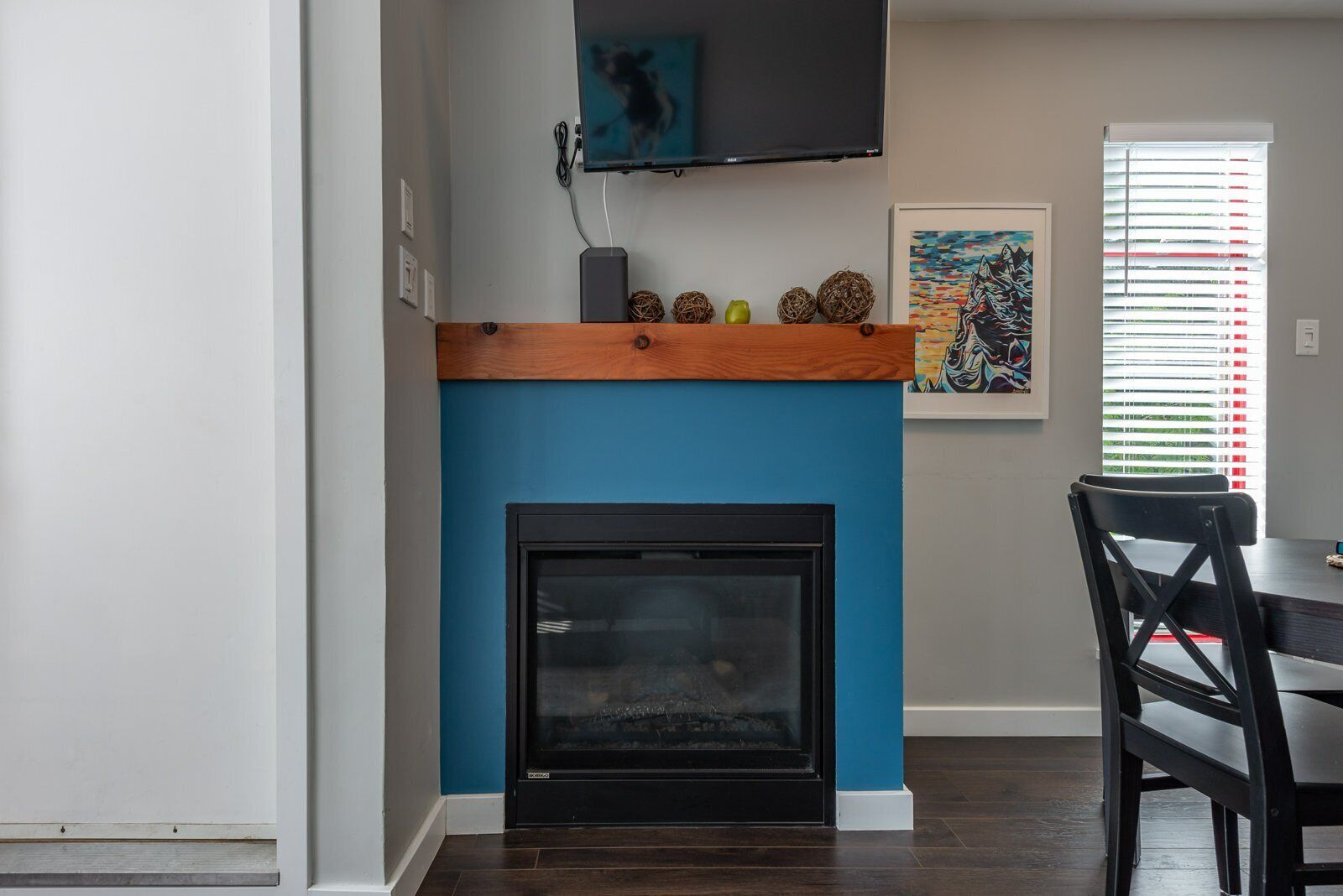 A modern living room with a blue accent wall, a fireplace, a mounted TV, and a dining area with a table and chairs.
