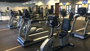 Une salle de sport équipée de nombreux appareils de cardio, notamment des tapis de course et des vélos elliptiques, disposés en rangées.