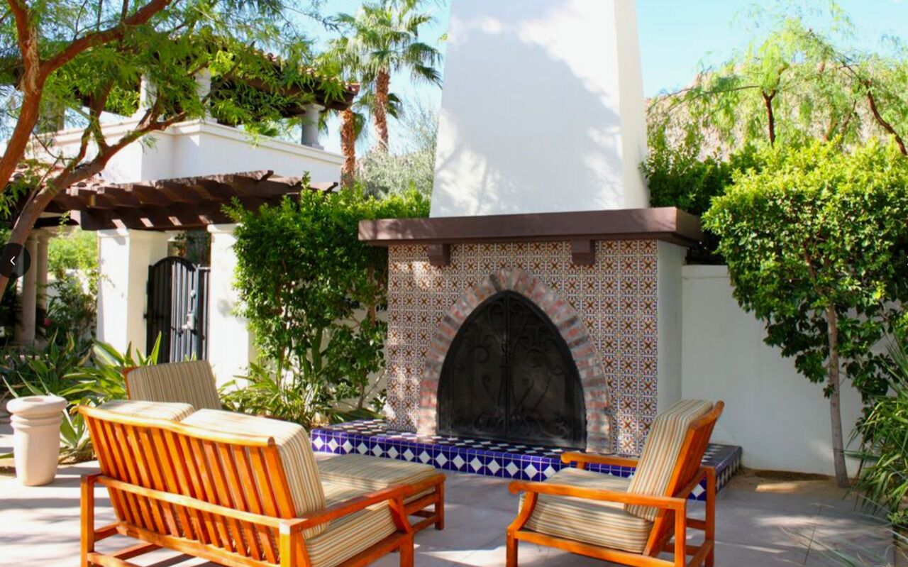 A patio with two wooden chairs and a tiled fireplace.