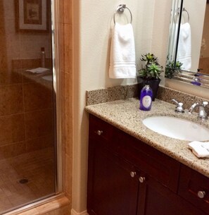 Une salle de bain avec un comptoir en granit, un lavabo blanc, un miroir et une plante en pot.