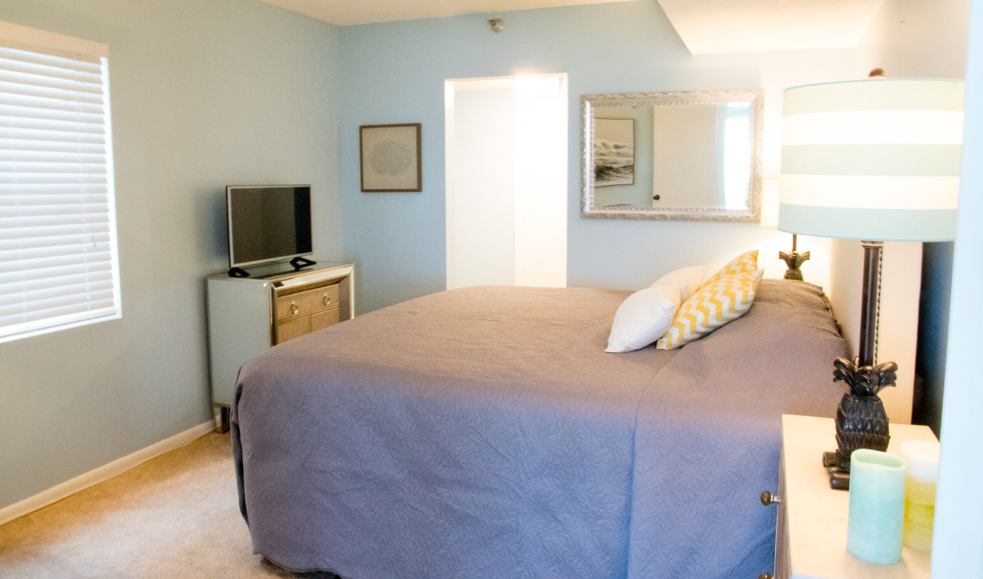 A bedroom with a large bed, a dresser, a television, and a mirror on the wall.