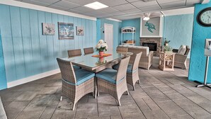A dining area with a glass-top table surrounded by wicker chairs with blue cushions, a white door, and a wall clock.