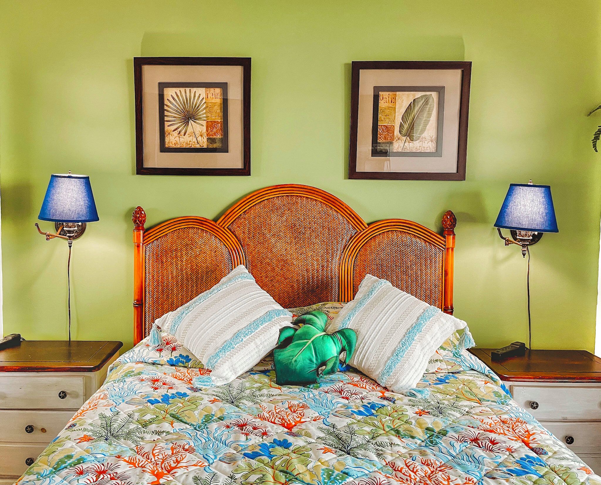 Un lit recouvert d’une couvre-lit à motifs floraux, deux tableaux encadrés accrochés au mur et deux lampes de chaque côté.