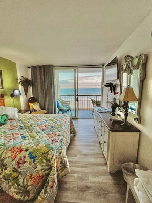 A hotel room with a bed, a desk, a chair, a lamp, and a view of the ocean. - Oceanfront Waterpointe1 504-3b/2b-Sleeps 6-Balcony-WIFI-TV-Pool-Family Friendly (North Myrtle Beach)