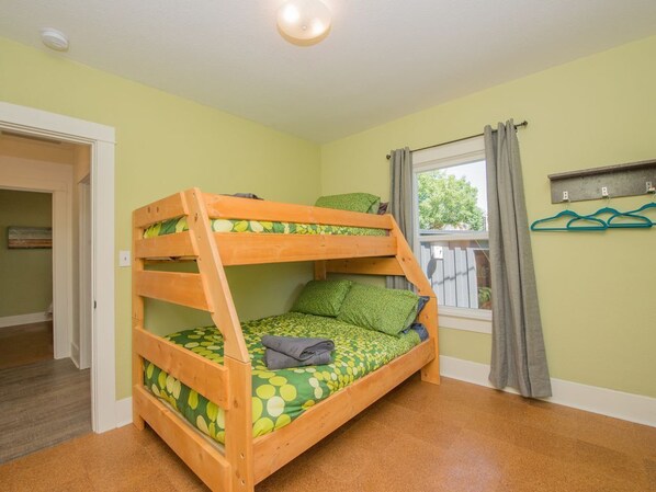 Un lit superposé dans une pièce avec une fenêtre, une porte et un porte-manteau avec des cintres.