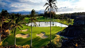Un parcours de golf avec un étang, des palmiers et une chaîne de montagnes en arrière-plan.