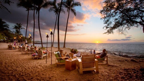A beach with wooden chairs and tables, palm trees, and a sunset over the ocean. -  Salt Water Pool⛱️  Ocean View 🌊 Hualalai View🌋 140+ 5 Star Reviews 🌟🌟🌟🌟🌟 (Waikoloa Village)
