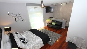 Ein modernes Schlafzimmer mit einem Bett, einer Sitzecke mit einer Couch, einem an der Wand montierten Fernseher und einem Deckenventilator.