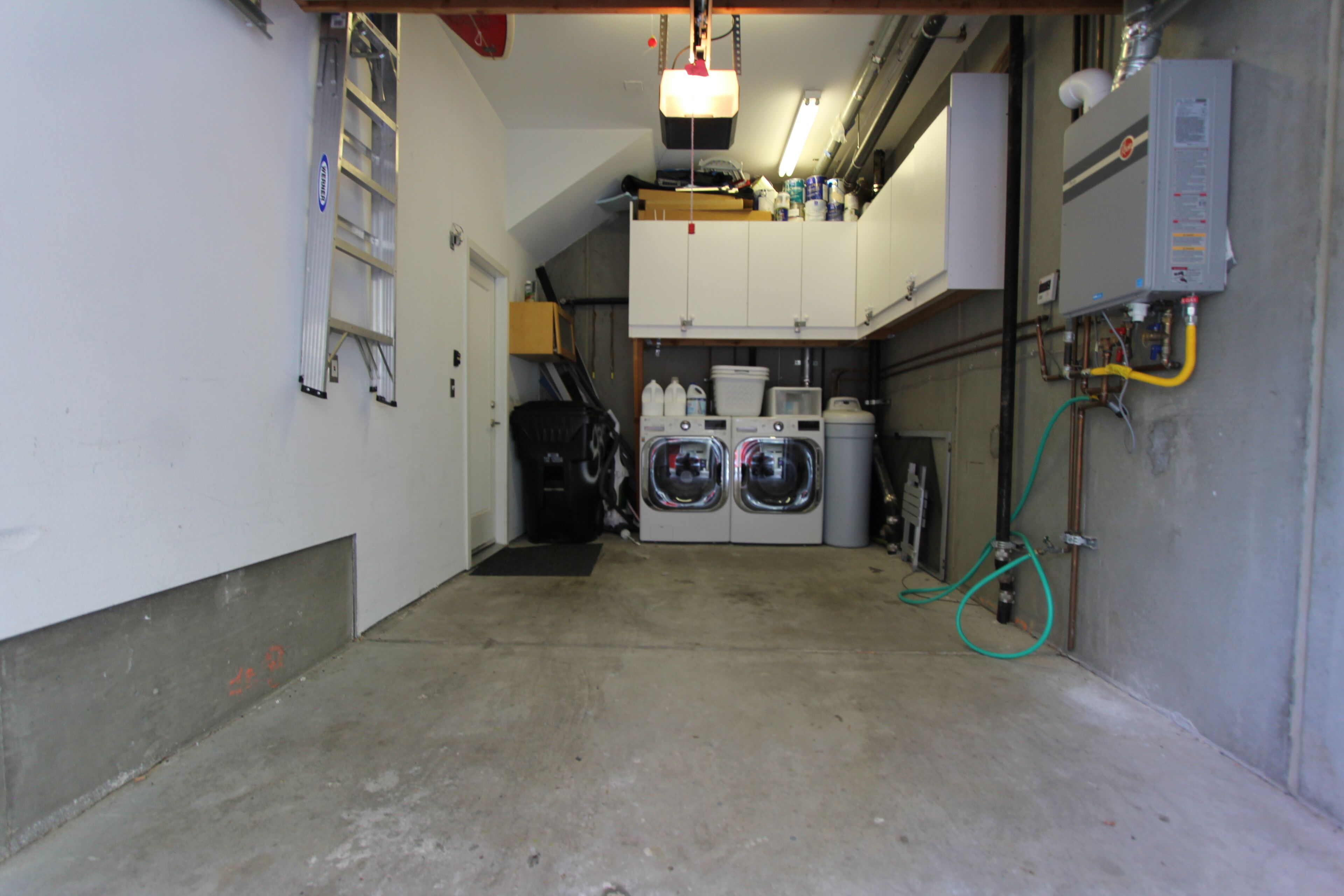 A laundry room with two front-loading washing machines, a dryer, and a water heater.