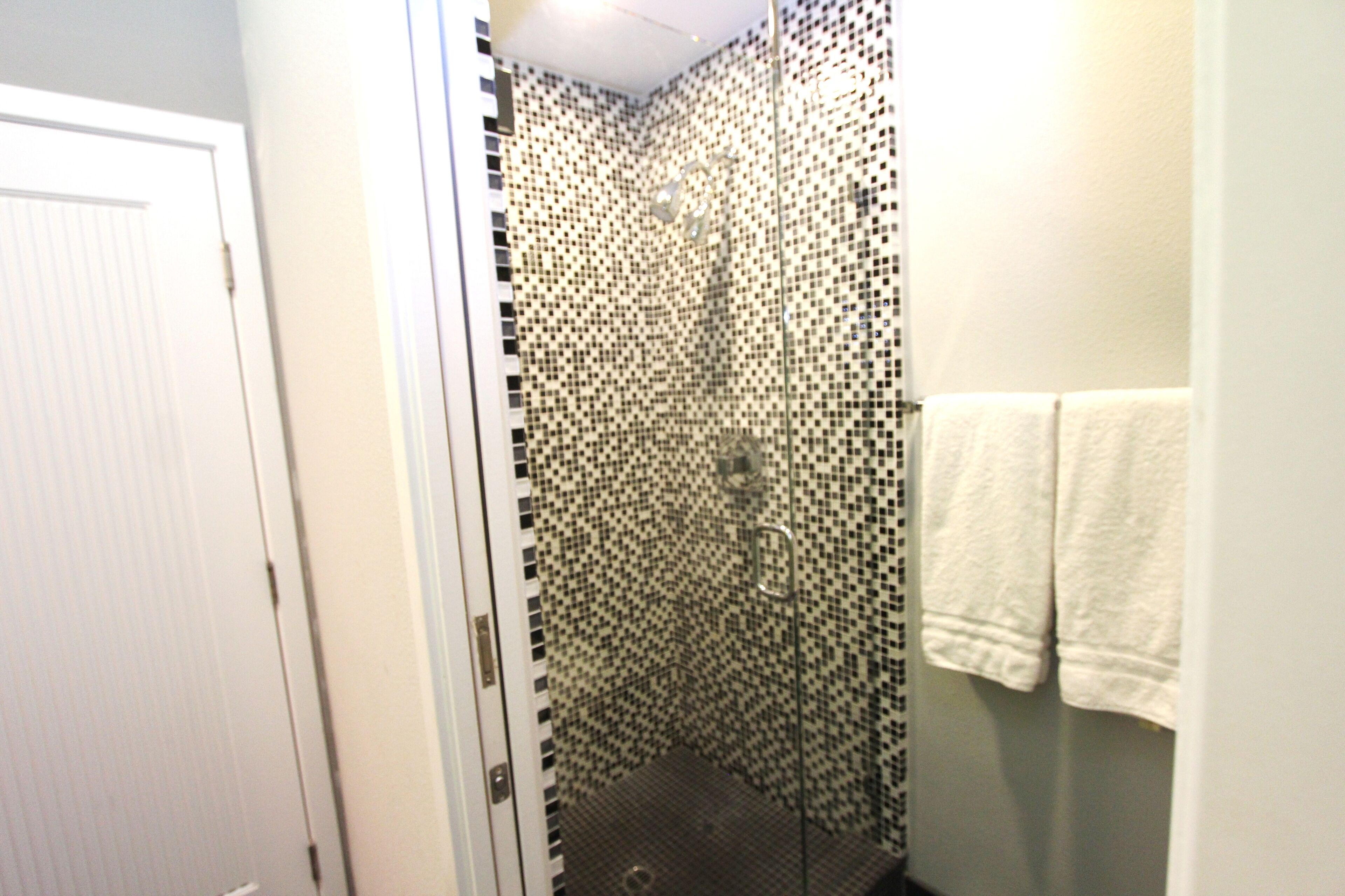Een badkamer met een douchegedeelte, een mozaïek betegelde muur, een glazen deur en een witte handdoek aan de wand.