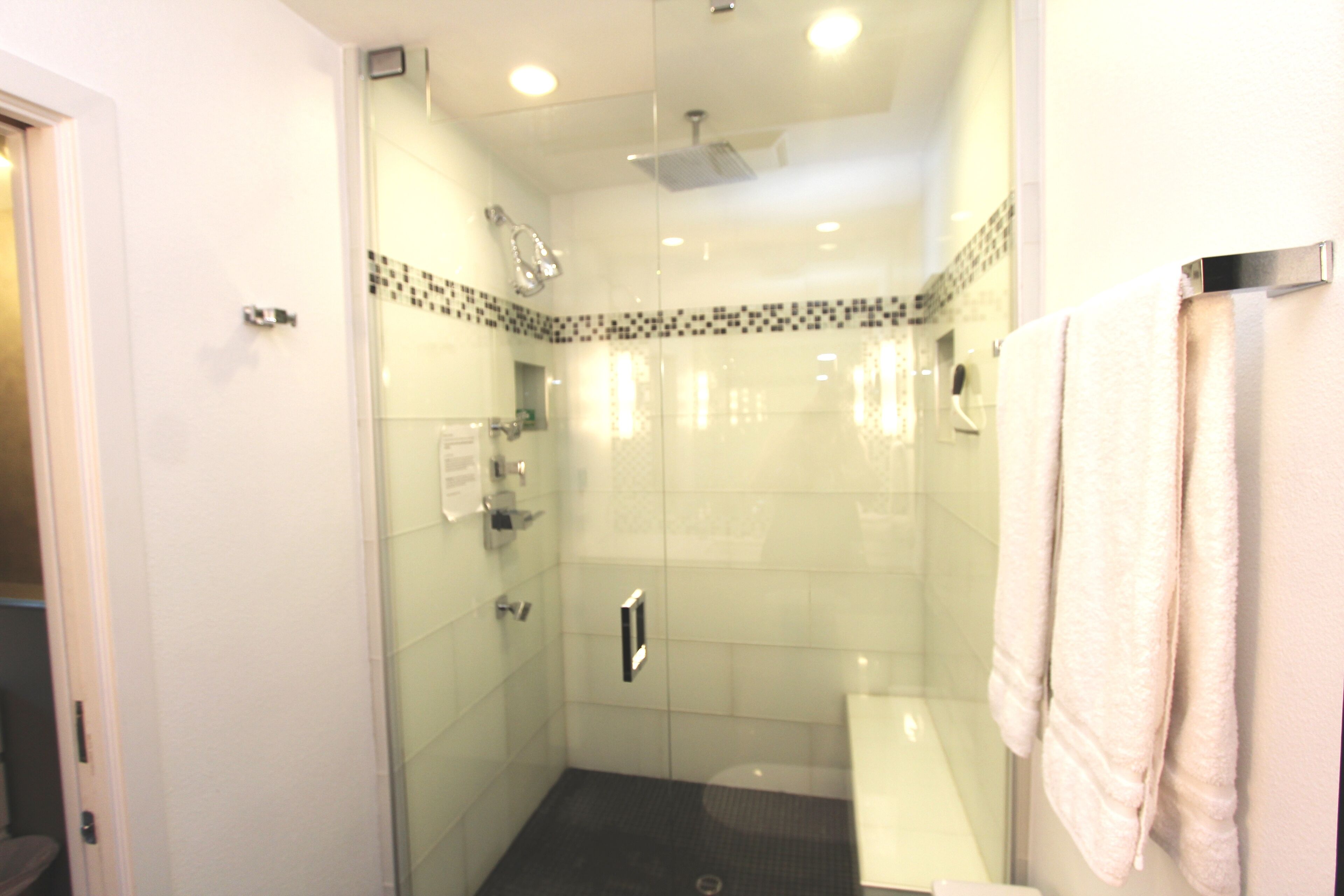 A glass-enclosed shower with a white tiled wall, a glass door, and a towel hanging on the wall.