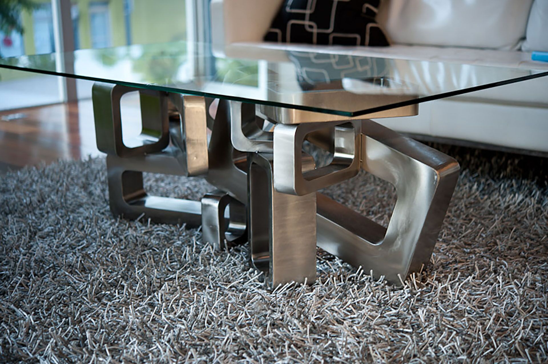 Ein moderner Tisch mit Glasplatte und Metallbeinen auf einem strukturierten Teppich.