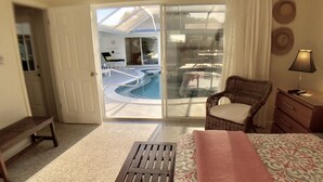 A hotel room with a bed, a wooden bench, a wicker chair, a desk with a lamp, and a view of a swimming pool through a glass door. - 4 BR/3BA Poolhouse is 4 miles from the famous Siesta Key Beach (Sarasota)