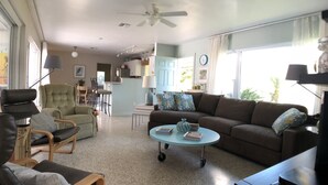 A spacious living room with a brown sofa, a green armchair, and a coffee table. There is a dining area in the background with a table and chairs. - 4 BR/3BA Poolhouse is 4 miles from the famous Siesta Key Beach (Sarasota)