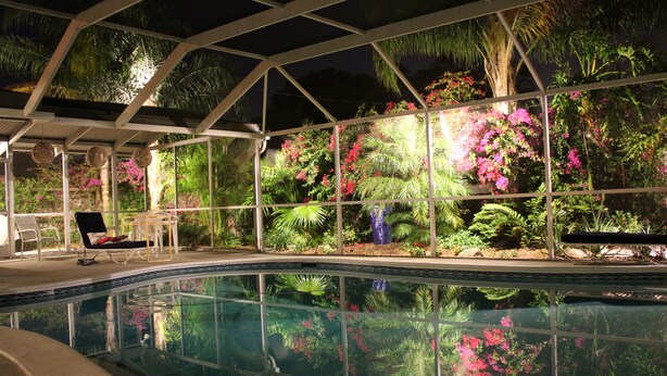 An indoor swimming pool with a glass enclosure, surrounded by lush tropical plants and flowers. - 4 BR/3BA Poolhouse is 4 miles from the famous Siesta Key Beach (Sarasota)