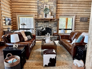 Cozy cabin interior with a stone fireplace, leather sofas, and a patterned rug.