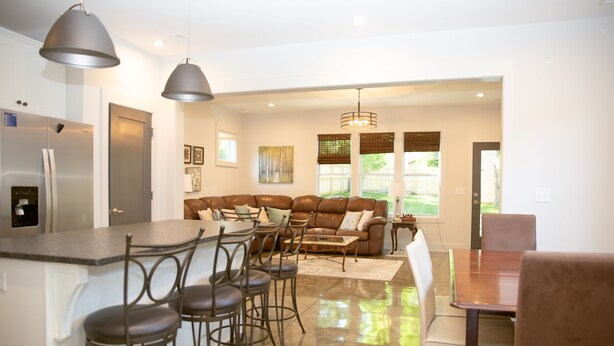Een moderne keuken met een centraal eiland, barkrukken, een eettafel en een zithoek met een bank en stoelen.