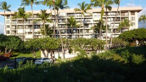 A multi-story hotel with balconies, surrounded by palm trees and greenery. - Enthralling Sunset Views from Top-floor Remodel steps from Maui's Best Beaches. (Kihei)