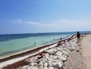 A beach with clear turquoise water, rocky shore, and people swimming and walking along the shore.