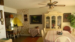Un comedor con mesa, sillas, ventilador de techo y un mueble con puertas de vidrio.