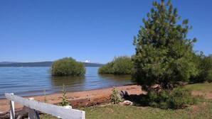 Vista de un lago con un banco de madera, un pino y una montaña distante.