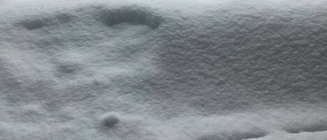 Een sneeuwbedekt terras met een houten hek en een sneeuwbedekte boom op de achtergrond.