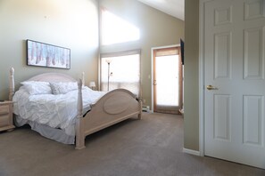 A bedroom with a four-poster bed, a nightstand, a bedside table, a lamp, and a door.