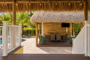 A covered outdoor area with a pool, lounge chairs, a dining table, and a TV mounted on the wall.