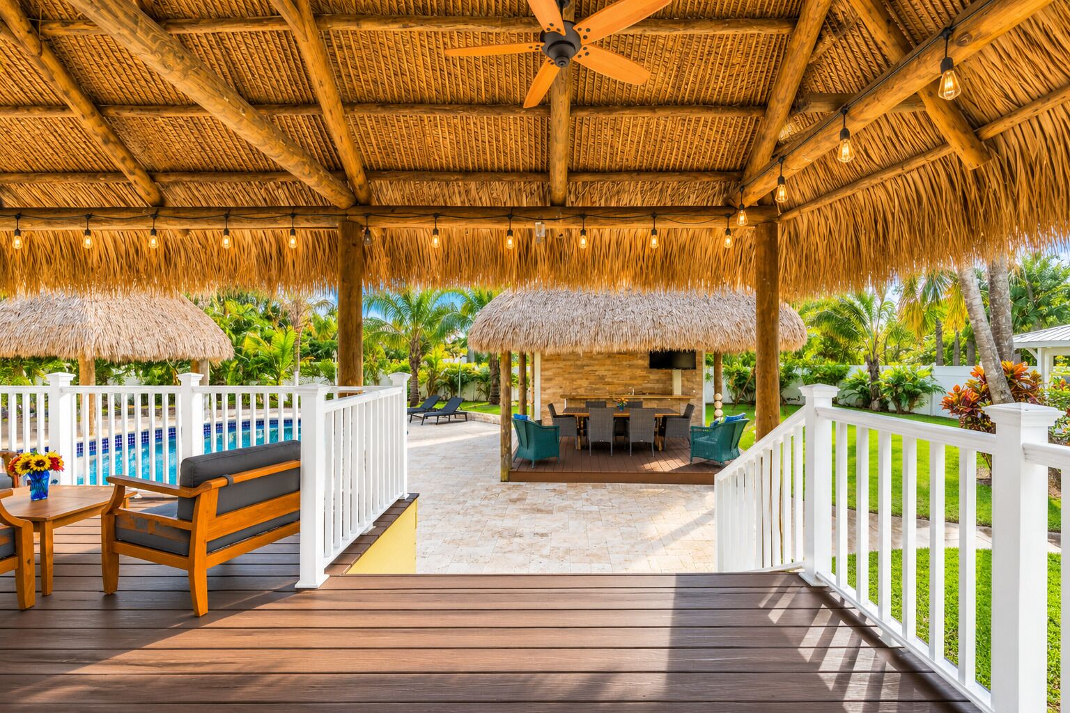 A covered outdoor area with a pool, seating, and a thatched roof.