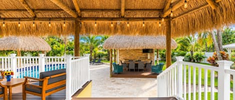 A covered outdoor area with a pool, seating, and a thatched roof.