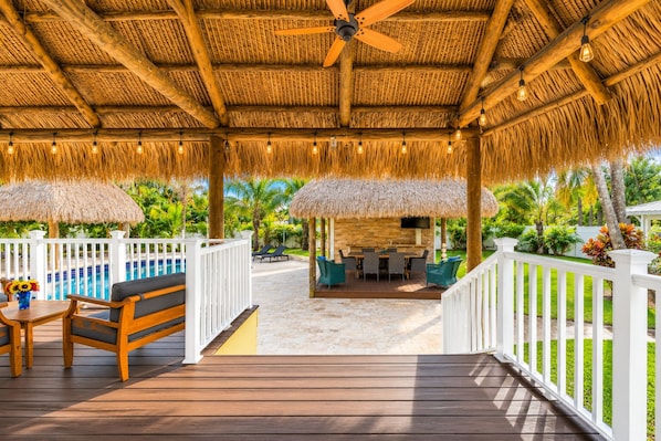 A covered outdoor area with a pool, seating, and a thatched roof.