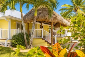A yellow building with a thatched roof, white railings, and a staircase leading to a porch.