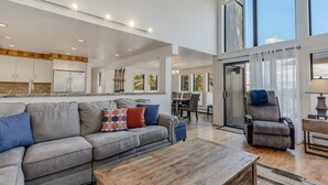 A spacious living area with a grey sofa, a wooden coffee table, and a dining area with a table and chairs. - Seconds to mall and slope, 2 hot tubs,1 pool, small gym, fireplaces (Snowmass Village)